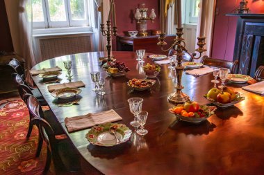 Bronx, NY - US - July 13, 2024 The dining room of Bartow Pell Mansion showcases a polished table with ornate candelabras, fine china, and fruits. Elegant decor and natural light enhance its charm. clipart