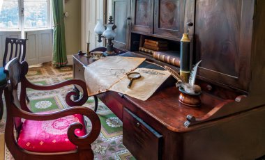 Bronx, New York - ABD - 13 Temmuz 2024 Bartow-Pell Malikânesi 'nin masasında antika gözlükler, bir büyüteç ve gazetelerde bir tüy kalemle tarihi cazibe sergileniyor. Antika kitaplar ve zarif dekorlar sahneyi tamamlıyor..