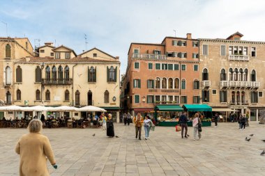 Venedik, Vento bilişim teknolojisi 14 Ekim 2024 Venedik 'te Grand Canal boyunca kenetlenmiş, gösterişli bir gondolcunun içinde duran bir gondolcu. Sudan yükselen uzun ahşap demirleme direkleri, canlı binaları çerçeveliyor..