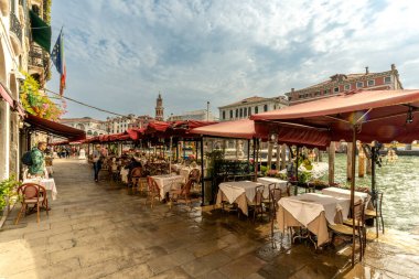 Venedik, Vento bilişim teknolojisi 14 Ekim 2024 Venedik 'te Grand Canal boyunca kenetlenmiş, gösterişli bir gondolcunun içinde duran bir gondolcu. Sudan yükselen uzun ahşap demirleme direkleri, canlı binaları çerçeveliyor..