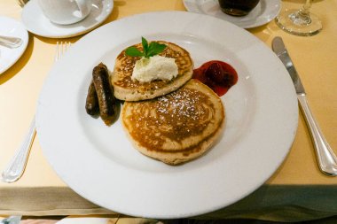 Erimiş tereyağı ve bir tutam nane ile kaplanmış yumuşak tereyağlı krep ızgara sosis ve bir tutam çilek sosu ile eşleştirilmiş, altın masa örtüsü üzerine yerleştirilmiş ince masa örtüsü..