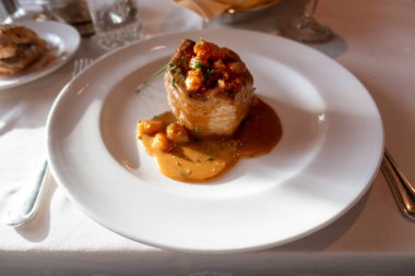 Deniz ürünleriyle dolu, kremalı sosla kaplı ve otlarla süslenmiş bir puf böreği, zengin bir kahverengi sosla beyaz bir tabakta servis ediliyor..