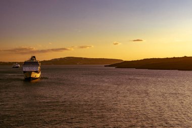 Santorini, Güney Ege - GR - 20 Ekim 202 Santorinis suları üzerinde nefes kesici bir gün batımı, altın renkler ufku kucaklarken ve bir yolcu gemisi huzur içinde Ege Denizi 'ne doğru yol alırken