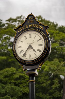 Paterson, NJ - ABD - 24 Mayıs 2025 Paterson, NJ 'deki Süslü Siyah ve Altın Sokak Saati 4: 35 gösteriyor. Bereketli yeşil ağaçlara karşı kurulmuş Paterson Est şehrini gururla ifade eder. 1792