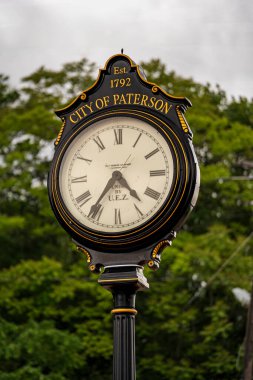 Paterson, NJ - ABD - 24 Mayıs 2025 Paterson, NJ 'deki Süslü Siyah ve Altın Sokak Saati 4: 35 gösteriyor. Bereketli yeşil ağaçlara karşı kurulmuş Paterson Est şehrini gururla ifade eder. 1792