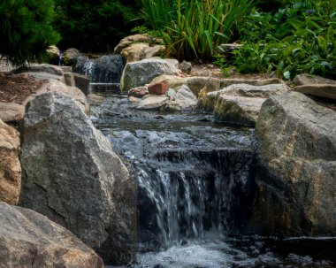 Yonkers, New York - ABD - 8 Haziran 2025 Untermyer Park 'taki Rock and Stream Garden doğal taşın üzerinde çağlayan su içeriyor, yemyeşil yapraklarla çevrili, barışçıl ve dalgın bir vaha yaratıyor..