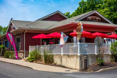 Highland, New York - ABD - 13 Haziran 2025 Donmuş Vagon, parlak kırmızı şemsiyeli canlı bir dondurma dükkanı, renkli bayraklar ve güneşli bir günde ziyaretçileri şeker yemeye davet eden dev bir girdap levhası.