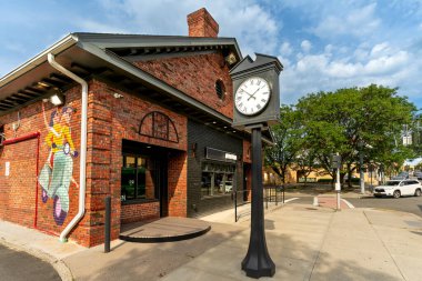 Acı içinde, New York - ABD - 21 Haziran 2025 Lavagna of Suffern 'ın dışında bir sokak saati duruyor. Cazibeli ve modern yetenekleriyle şehir merkezindeki bir köşede koyu renkli duvar resmi ve siyah bir dükkan var..