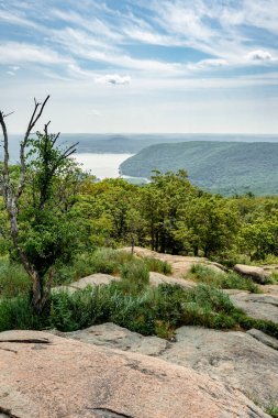 Stony Point, New York - ABD - 3 Haziran 2025 Bear Mountain State Park 'taki kayalık ve yüksek bir levrekten, manzaralı bir tepede ağaçlarla kaplı dağlar, Hudson Nehri ve bulutlarla kaplı puslu bir gökyüzü görülüyor..