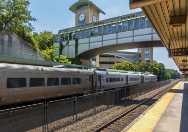 Ramsey, NJ - ABD - 6 Temmuz 2025 Ramsey Route 17 İstasyonu 'ndaki metro-kuzey treni modern bir saat kulesi gökdeleni ve New Jersey' nin kuzeyindeki açık mavi gökyüzü altında yaz yeşili çerçeveli..