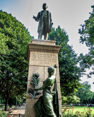Bronx, New York - ABD - 16 Ağustos 2025 'te Joyce Kilmer Park, Bronx' ta Louis J. Heintz 'ın Yeşillik ve çiçek açan kırmızı güller tarafından çerçevelenen semtin kuruluşunu, ilerlemesini ve refahını onurlandıran heykeli.