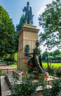 Bronx, New York - ABD - 16 Ağustos 2025 'te Joyce Kilmer Park, Bronx' ta Louis J. Heintz 'ın Yeşillik ve çiçek açan kırmızı güller tarafından çerçevelenen semtin kuruluşunu, ilerlemesini ve refahını onurlandıran heykeli.