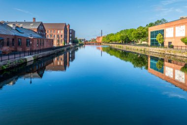 Holyoke, MA-ABD - 24 Ağustos 2025 Sakin bir kanal, kırmızı tuğlalı sanayi binalarını ve Holyoke 'de dağınık mavi bulutların altında bir köprüyü yansıtır.