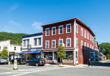 Shelburne Falls, MA - ABD - 23 Ağustos 2025 Shelburne Falls şehir merkezi caddesi kırmızı ve mavi tarihi dükkanları kaldırım kenarına park etmiş arabalar ve açık gökyüzü altında yaya geçidi.