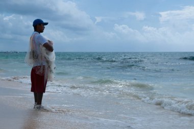 Sabahın ilk ışıklarıyla birlikte genç bir balıkçı denize dökme ağıyla fırlatmak için doğru zamanı bekliyor, Playa del Carmen, Meksika
