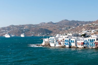 Yunan adası Mykonos 'taki Chora köyünün panoramik manzarası, arka planda kayalık tepeler ve demirli yolcu gemileri. Akdeniz tatil seyahati kavramı