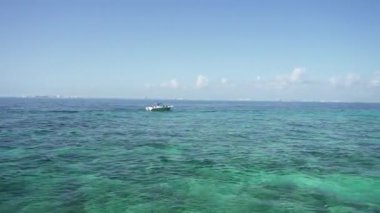 Isla Mujeres 'in güneşli güney sahillerine kristal berrak Karayip Denizi ile HD genel bakış, bir yaz günü kayalık sahil şeridi mavi gökyüzü boyunca bir tekne hareket eder. Seyahat ve tatil için ideal