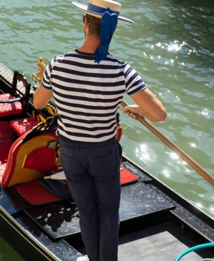 Venedik kanalında gondolcunun romantik bir turist rotasında kürek çekerken görüntüsü.