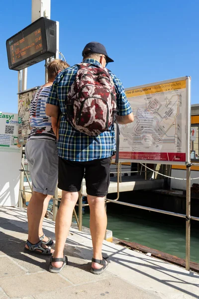 Üst düzey turist çifti, güneşli bir günde İtalya 'nın Venedik şehrinde su taşımacılığının haritası ve çizelgesi üzerinde çalışıyor.
