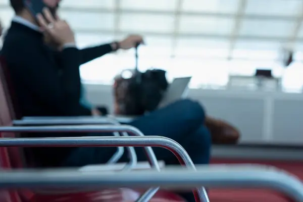 Havaalanı kapısında oturan bir adam uçuşunu beklerken kucağında telefon ve dizüstü bilgisayarla konuşuyor. Paris, Fransa. Seçici odak