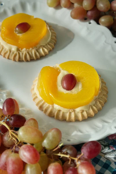 Two individual peach tarts on a white porcelain platter. Table grapes placed on the sides of the plate.