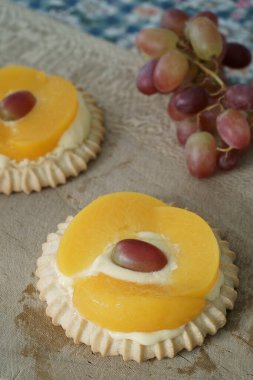 Tahta kesme tahtasının üzerinde iki ayrı şeftali turtası ve üzüm. Arka planda mavi ve beyaz bir masa örtüsü.