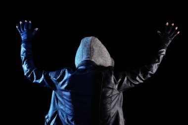 Deri ceket giyen ve elleri havada kapüşon giyen kişi arkadan görülüyor. Siyah arkaplanda izole.