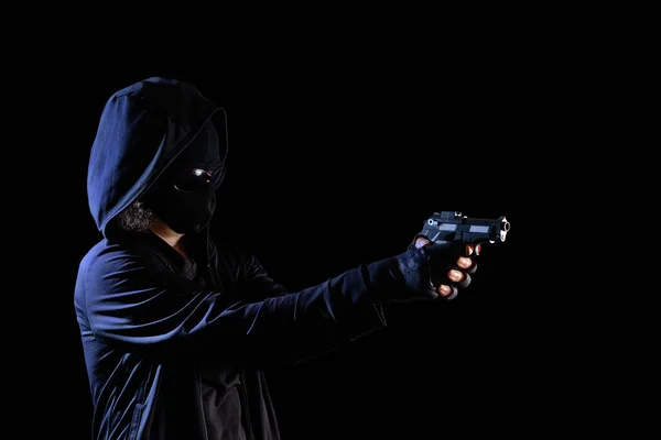 Masked person pointing a handgun, ready to shoot. Isolated on a black background.