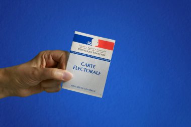 Fransız oy kartını tutan bir el. Mavi desenli arkaplan.