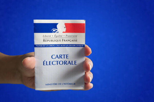 A hand holding a French voting card. Blue textured background.