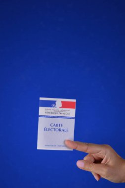 Fransız oy kartını tutan bir el. Mavi desenli arka plan. Boşluğu kopyala.