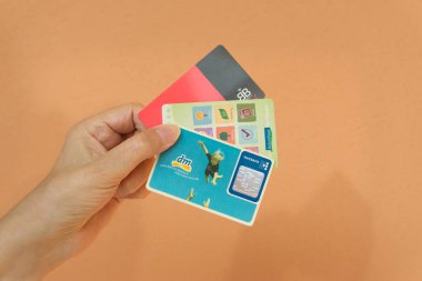 Alman mağazasının sadakat kartlarını tutan bir el. Arka planda turuncu duvarın açık tonu.