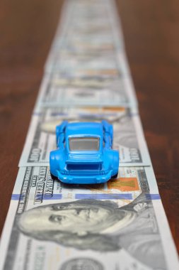 100 dolarlık banknotlardan yapılmış bir yolda bir Porsche oyuncak araba sürüyor. Koyu renk ahşap.