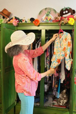 Yeşil gardırobundan renkli bir bluz seçen bir kadın. Hasır şapka ve yaz kıyafetleri giyiyor..