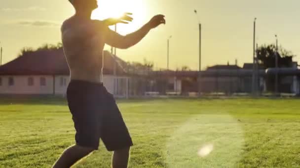 年轻男子日落时在体育场抛接足球 职业足球运动员在绿地踢球 运动员在草地上练习杂技 背景是阳光 自由式足球 — 图库视频影像