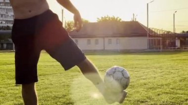 Yeşil sahada erkek futbolcu topa vuruyor. Gün batımında stadyumda futbol oynayan genç adamın bacakları. Sporcu dışarıda numaralar yapıyor. Serbest stil futbol