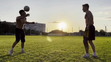 Sahada birbirlerine pas verirken iki sporcu topla numara yapıyor. Gençler gün batımında stadyumda futbol oynuyorlar. Meadow 'da profesyonel futbolcu eğitimi. Serbest stil futbol.