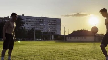 Sahada birbirlerine pas verirken iki sporcu topla numara yapıyor. Gençler gün batımında stadyumda futbol oynuyorlar. Meadow 'da profesyonel futbolcu eğitimi. Serbest stil futbol.