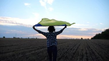 Ukraynalı bir kadın gün batımında kafasının üstünde Ukrayna bayrağıyla koşuyor. Bayan gün doğumunda ulusal mavi-sarı bayrak ile arpa çayırında koşuyor. Rus saldırısına karşı zafer.