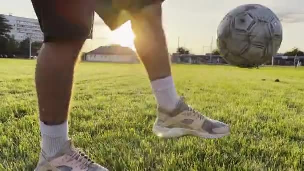 日没のスタジアムでサッカーボールをジャグリングする若者 グリーンフィールドでボールを蹴るプロサッカー選手 スポーツマンは バックグラウンドで日光でメドウでトリックを実践しています フリースタイルフットボール — ストック動画