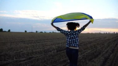 Ukraynalı bir kadın gün batımında kafasının üstünde Ukrayna bayrağıyla koşuyor. Bayan gün doğumunda ulusal mavi-sarı bayrak ile arpa çayırında koşuyor. Rus saldırısına karşı zafer.