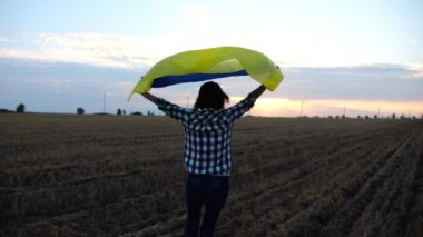 Ukraynalı bir kadın gün batımında kafasının üstünde Ukrayna bayrağıyla koşuyor. Bayan gün doğumunda ulusal mavi-sarı bayrak ile arpa çayırında koşuyor. Rus saldırısına karşı zafer.