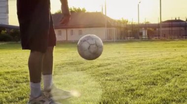 Yeşil sahada erkek futbolcu topa vuruyor. Gün batımında stadyumda futbol oynayan genç adamın bacakları. Sporcu dışarıda numaralar yapıyor. Serbest stil futbol