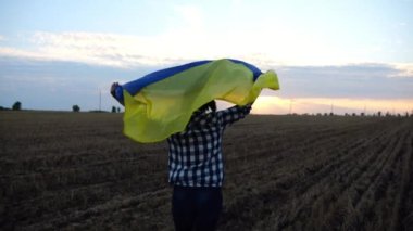 Ukraynalı bir kadın gün batımında kafasının üstünde Ukrayna bayrağıyla koşuyor. Bayan gün doğumunda ulusal mavi-sarı bayrak ile arpa çayırında koşuyor. Rus saldırısına karşı zafer.