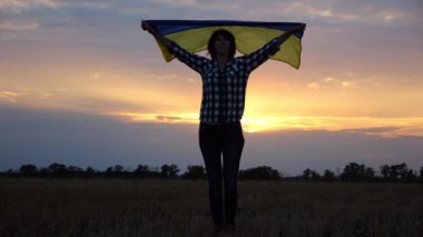 Arpa otlağında dikilen Ukraynalı bir kadın kafasında mavi-sarı bir afişle arka planda güzel bir günbatımında. Ukrayna bayrağını kaldıran kadın, Rusya 'nın saldırısına karşı zafer sembolü oldu.