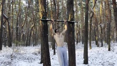 Güçlü ve kaslı bir adam kış ormanının yatay çubuğunda egzersiz yapıyor. Genç sporcu güzel doğada kaslarını geliştiriyor. Atletik adam dışarıda antrenman yapıyor. Spor ve aktif yaşam tarzı kavramı.