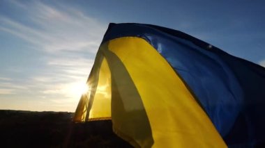 Güneş ışığının arka planında rüzgarda dalgalanan Ukrayna bayrağı. Ukrayna 'nın mavi-sarı sembolü. Kırsalda güneş parıldıyor. Rus saldırısına karşı barış ve destek kavramı.
