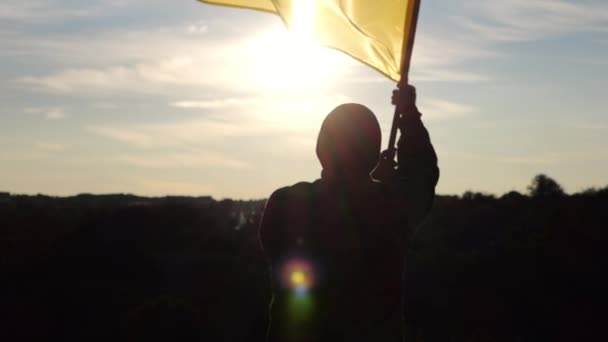 乌克兰人军人的肖像站在山岗上 挥动着国旗 挡住夕阳 男兵升起蓝黄色的旗帜 象征着对俄国侵略的胜利 争取独立 — 图库视频影像
