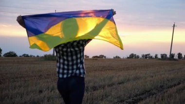 Arpa çayırında ulusal mavi-sarı pankartıyla koşan Ukraynalı kadın. Arka planda güzel bir günbatımı var. Gün batımında kafasının üstünde Ukrayna bayrağıyla koşan bir kadın. Yavaş