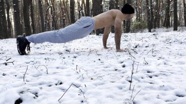Güçlü bir adam kış ormanında karda şınav çekiyor. Sporcu doğada egzersiz yapıyor. Genç adam dışarıda antrenman yapıyor. Kas sporcusu sıkı ve yoğun idman yapıyor. Sportif yaşam tarzı kavramı.